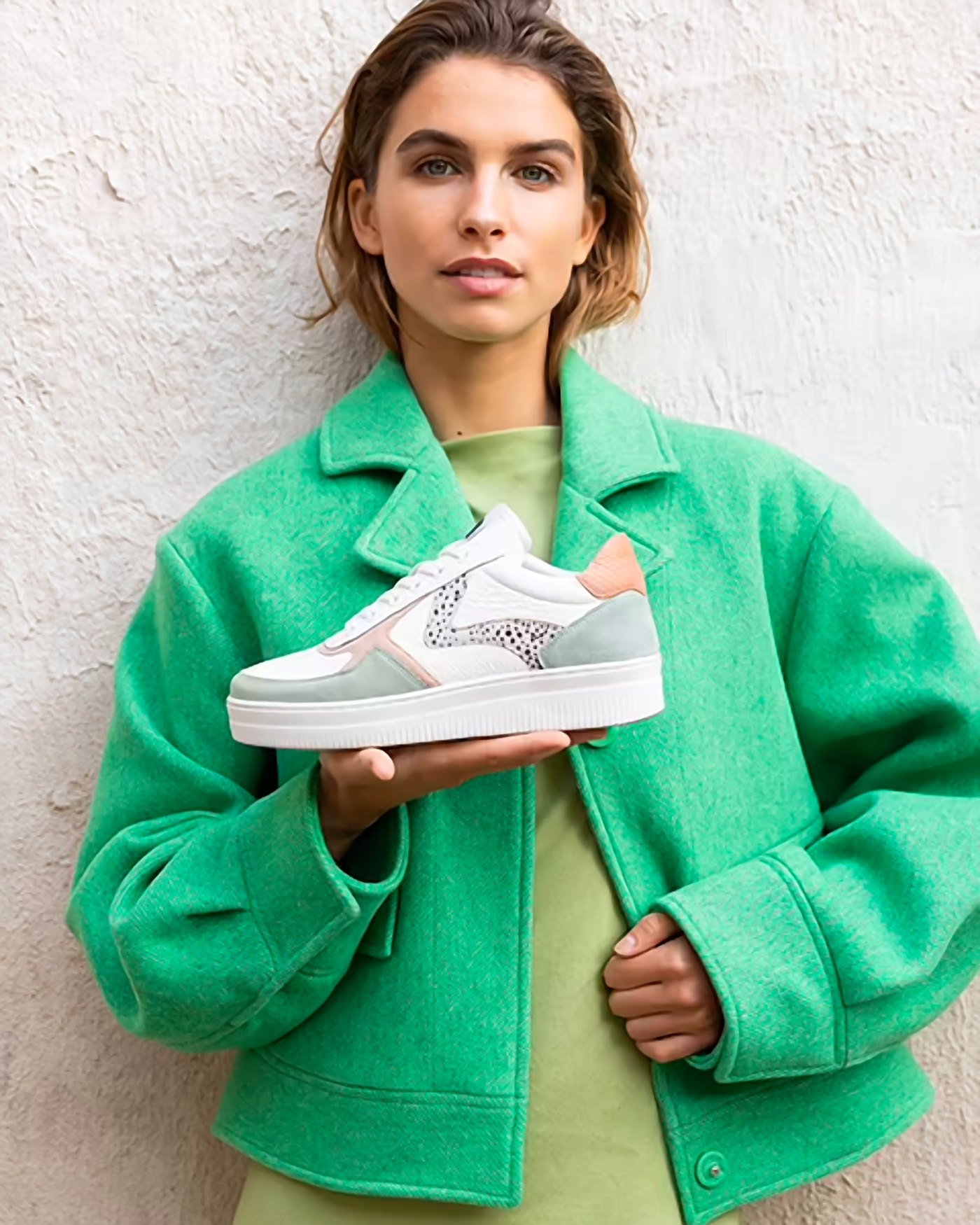 Model in a green jacket holding a Maruti sneaker